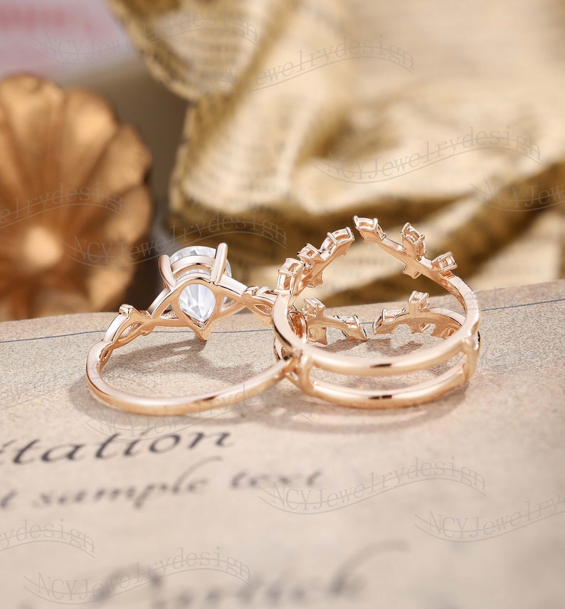 May include: A set of two rose gold rings with a pear-shaped diamond in the center of the larger ring. The smaller ring has a delicate leaf design.