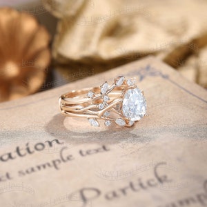 May include: A pear-shaped diamond engagement ring set in rose gold with a delicate, vine-like band adorned with smaller diamonds. The ring is set on a vintage-looking book with the text "Partick" visible.