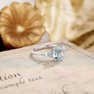May include: A silver ring with an oval-shaped aquamarine gemstone surrounded by smaller diamonds. The ring is set on a white background.