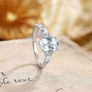 May include: A silver ring with a light blue oval-shaped gemstone surrounded by smaller, clear gemstones.
