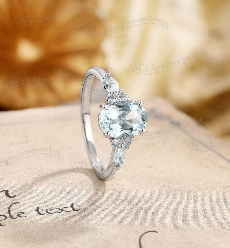 May include: A silver ring with a light blue oval-shaped gemstone surrounded by smaller, clear gemstones.