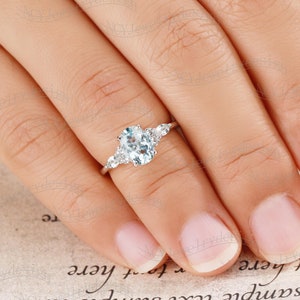 May include: A silver engagement ring with an oval-shaped aquamarine center stone and smaller round diamonds on the band.