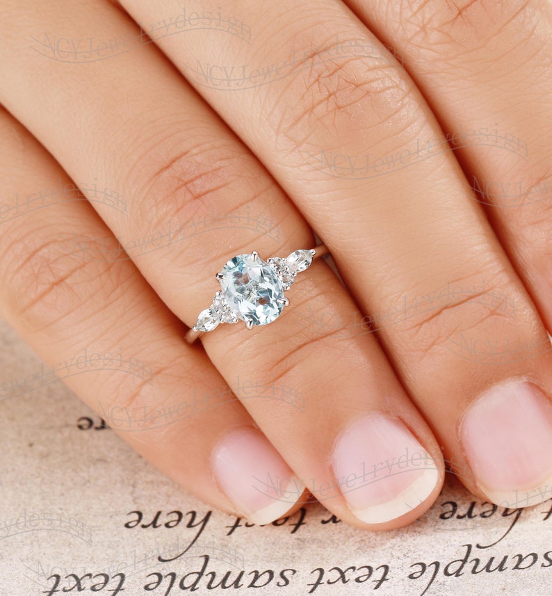 May include: A silver engagement ring with an oval-shaped aquamarine center stone and smaller round diamonds on the band.