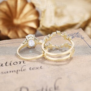 Op de afbeelding: Twee gouden ringen met heldere edelstenen. De grotere ring heeft een ovale edelsteen die omringd is door kleinere edelstenen. De kleinere ring heeft een delicaat ontwerp met kleine edelstenen.