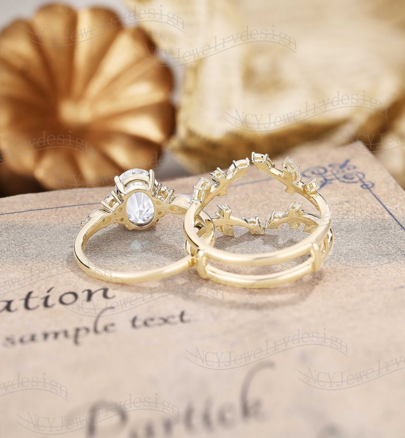 Op de afbeelding: Twee gouden ringen met heldere edelstenen. De grotere ring heeft een ovale edelsteen die omringd is door kleinere edelstenen. De kleinere ring heeft een delicaat ontwerp met kleine edelstenen.
