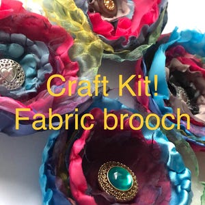 Puede incluir: Un kit de manualidades para hacer broches de tela. Los broches están hechos de tela colorida en tonos rosa, azul y amarillo. Cada broche presenta un botón decorativo con un corazón o una joya.