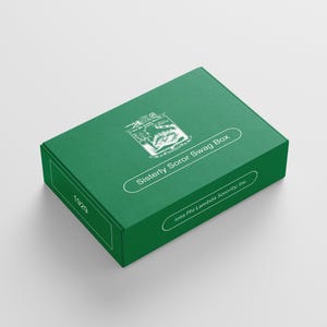 May include: A green rectangular box with white text that reads "Sisterly Soror Swag Box" and "Iota Phi Lambda Sorority, Inc." A white emblem is on the top of the box, and the number "1929" is on the side.