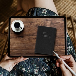 Pode incluir: Uma tela de tablet mostrando uma superfície de madeira com uma xícara de café e um caderno preto com o texto "MUSIC SCHOOL" nele. Uma caneta branca está na tela.