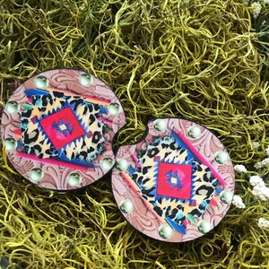May include: Two round brown coasters with a colorful geometric pattern and leopard print. The coasters have a beaded border and are perfect for adding a touch of southwestern style to your home decor.