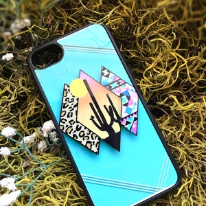 May include: A turquoise phone case with a geometric design featuring a cactus, a sun, and a leopard print pattern.