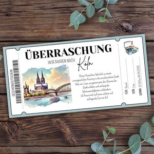 Könnte beinhalten: Ein blauer und weißer Geschenkgutschein mit dem Text "Überraschung" und "Wir fahren nach Köln". Der Gutschein zeigt eine Aquarellillustration des Kölner Doms und einer Brücke über den Rhein.