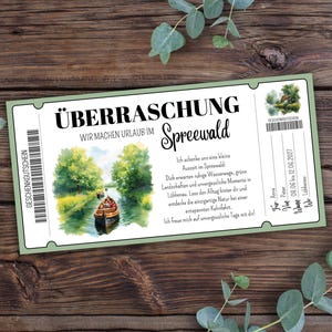 Może przedstawiać: Bon upominkowy z zieloną obwódką i niemieckim tekstem "ÜBERRASCHUNG Spreewald". Zawiera akwarelę przedstawiającą łódź na rzece. Bon leży na drewnianym tle z liśćmi eukaliptusa.