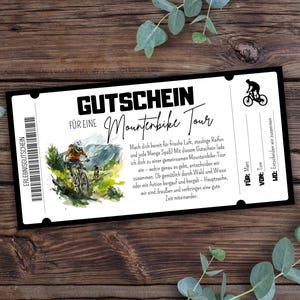 Op de afbeelding: Een zwart-wit cadeaubon met de woorden "GUTSCHEIN" en "Mountainbike Tour" in vette letters. De bon bevat een illustratie van een mountainbiker en een barcode. De tekst is in het Duits.