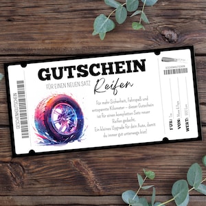 May include: A black and white gift certificate with the text "GUTSCHEIN" and "Reifen" in large font. The certificate features a colorful illustration of a car tire and text in German. The certificate is on a dark wood surface.