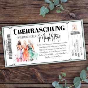 Könnte beinhalten: Ein Geschenkgutschein mit den Worten "ÜBERRASCHUNG Wir machen einen Mädelstrip" in schwarzem Text. Der Gutschein zeigt eine Illustration von drei Frauen in bunten Kleidern. Der Hintergrund ist eine Holzoberfläche mit grünen Blättern.