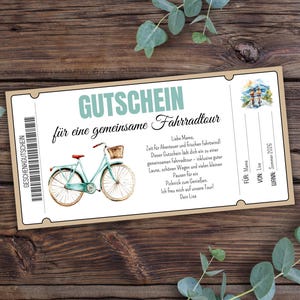 Op de afbeelding: Een lichtbruine cadeaubon met een blauwe fiets illustratie en de tekst "GUTSCHEIN für eine gemeinsame Fahrradtour" in het Duits. De tekst onder de fiets luidt "Liebe Mama, Zeit für Abenteuer und frischen Fahrtwind! Dieser Gutschein lädt dich ein zu einer gemeinsamen Fahrradtour - inklusive guter Laune, schönen Wegen und vielen kleinen Pausen für ein Picknick zum Genießen. Ich freu mich auf unsere Tour! Dein Lisa" in het Duits.
