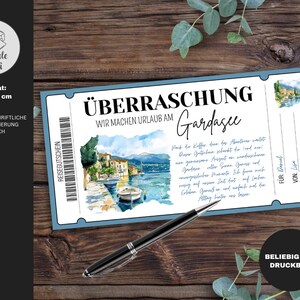 以下が含まれることがあります： 「&Uuml;BERRASCHUNG WIR MACHEN URLAUB AM Gardasee」のテキストが入った、青と白のチケットスタイルのバウチャー。バウチャーには、ボートや建物のある湖のシーンの水彩画イラストが描かれています。黒いペンが木製の表面に置かれています。