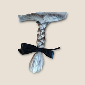 May include: A silver-grey braid with a black satin ribbon tied around it. The braid is attached to a piece of netting.