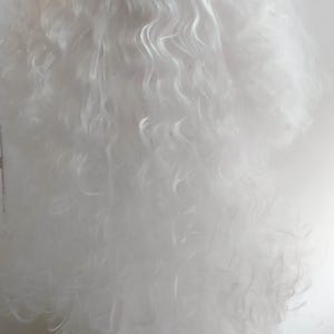 May include: A long, white Santa Claus beard and mustache set. The beard is full and fluffy with a slightly wavy texture. The mustache is neatly trimmed and attached to the upper lip area. Ideal for festive costumes.