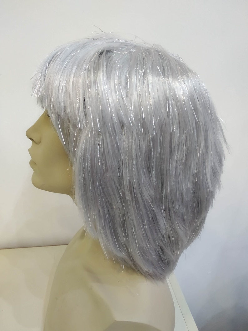 May include: A gray wig with silver tinsel strands, styled in a short, layered bob. The wig is displayed on a mannequin head, showcasing the side profile of the hair's texture and shape. The wig's color is a light gray.