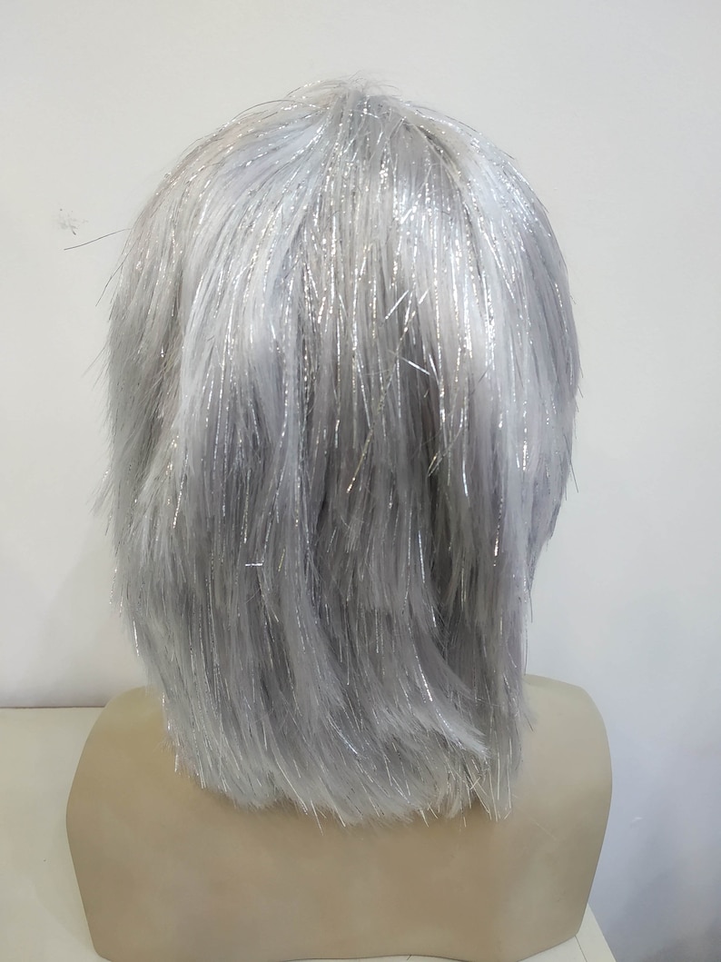 May include: A gray wig with silver tinsel strands, styled in a short, layered cut. The wig is displayed on a mannequin head. The hair has a slightly textured appearance, with the silver strands adding a touch of sparkle.