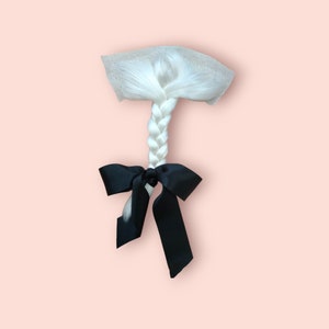 May include: A white braid with a black satin ribbon tied at the end. The braid is attached to a mesh base.