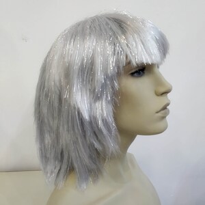 May include: A silver wig with a blunt fringe, displayed on a mannequin head. The wig has a short, layered style with strands of silver tinsel throughout, creating a shimmering effect. The mannequin has a neutral skin tone and is set against a white background.