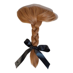 May include: A long, braided, light brown hair extension with a black ribbon tied in a bow at the end.