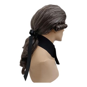 Op de afbeelding: Een grijs en wit pruik in de stijl van de 18e eeuw, met gekrulde zijkanten en een lange paardenstaart vastgemaakt met een zwart lint. Het wordt gedragen met een zwart halsstuk, ideaal voor historische re-enactments of kostuumevenementen.