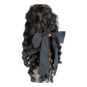 May include: A black wig with long, curly hair styled in a large bun with a black satin bow.