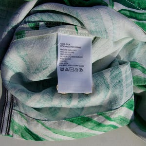 May include: Close-up of a silk fabric with a green and white striped pattern. A white tag with care instructions is attached. The tag reads "100% Silk Copyrighted Print". The fabric is soft and appears to be part of a garment.