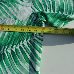 May include: A white and green tropical print shirt with a palm leaf design. A yellow measuring tape is placed across the fabric, showing a measurement of approximately 66 cm.