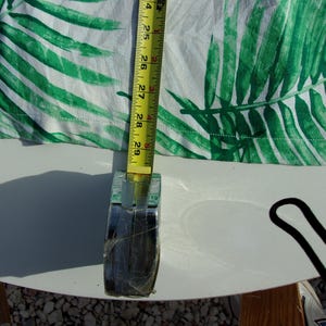 May include: White fabric with a green palm leaf pattern is measured with a yellow tape measure. The tape measure shows a measurement of 61 to 74 cm. The fabric is on a white surface.