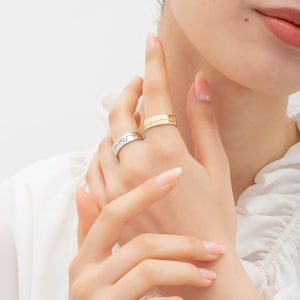 May include: Two gold and silver rings with engraved text. The rings are worn on the index finger of a hand.