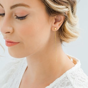 May include: Gold star-shaped earrings with a long, thin chain dangling from the bottom. The earrings are worn by a person with blonde hair.