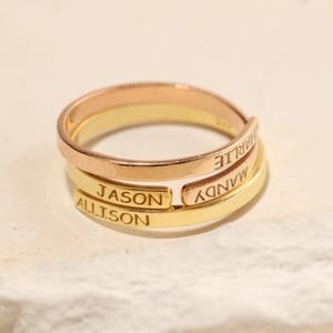 May include: A gold, silver, and rose gold ring with the names "Mandy", "Charlie", "Jason", and "Allison" engraved on it.