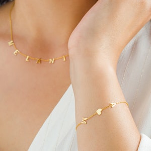 May include: A gold necklace with the name "MELANI" spelled out in individual letters. A gold bracelet with the letters "M" and "A" and a heart charm.