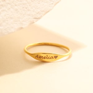 以下が含まれることがあります： 「アメリア」という名前と小さなハートのシンボルが刻まれた金色のリングです。