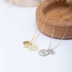May include: Two delicate necklaces with personalised charms. One gold necklace features three charms: an infinity symbol, the word "love", and a charm with the initials "K & G". The other silver necklace has two charms: a round charm with the word "forever" and a small heart charm.
