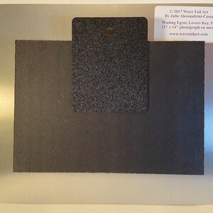 May include: A metal photograph with a silver border and a black backing. The photograph is labeled "Wading Egret, Lovers Key, FL" and measures 11 x 14 inches. The back has a black textured rectangle with a hole for hanging. The artist's name and website are also visible.