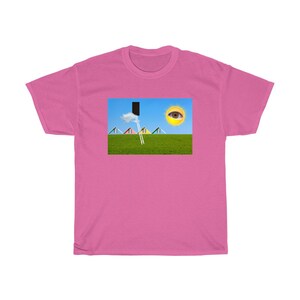 May include: A pink t-shirt featuring a surreal landscape design. The graphic includes a green field, blue sky, a ladder leading to a black rectangle, a cloud, and a sun with an eye. The design also includes colorful triangular shapes.