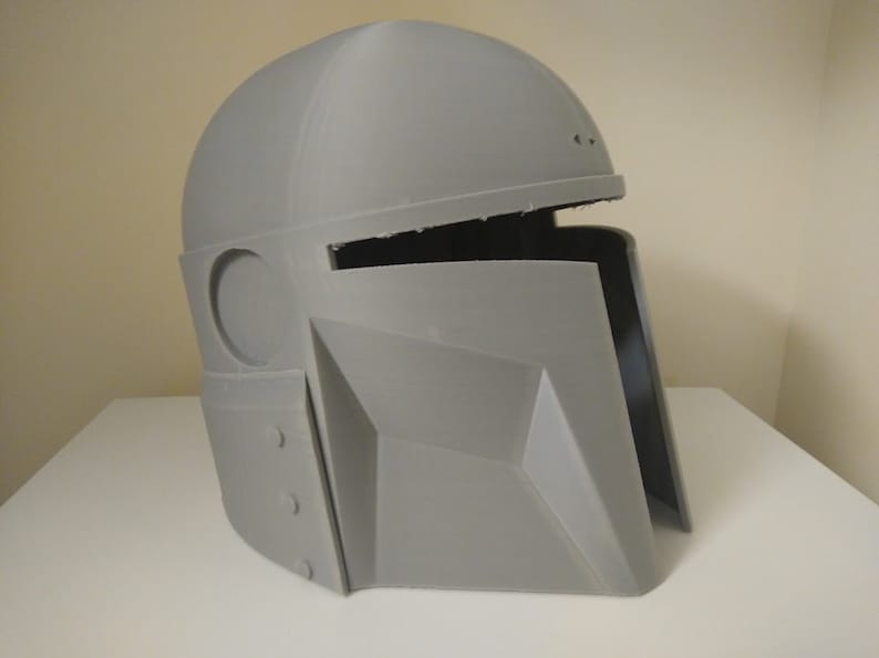 May include: A grey 3D printed helmet with a visor and a round opening on the side. The helmet is made of plastic and has a textured surface.