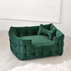 May include: A deep green velvet dog bed with a tufted design and a matching bone-shaped pillow. The bed is rectangular and has a raised edge.