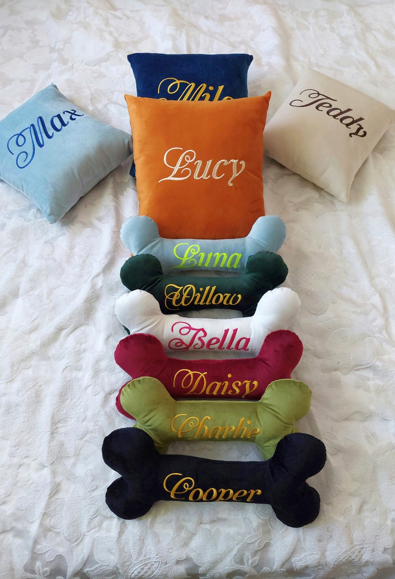 May include: A set of 9 personalized dog bone pillows. The pillows are in various colors and feature embroidered names, including Max, Lucy, Teddy, Luna, Willow, Bella, Daisy, Charlie, and Cooper.
