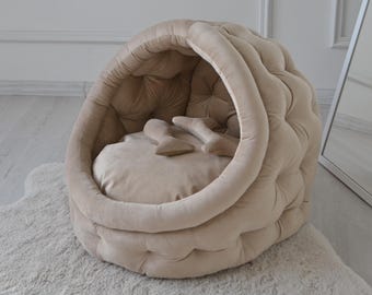 May include: A beige plush dog bed shaped like a dome with a soft, cushioned interior. The bed has a tufted design and a rounded opening for easy entry.