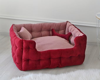 May include: A red and pink dog bed with a tufted design. The bed has a raised edge and a soft, plush lining.