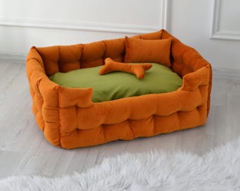 May include: Orange and green dog bed with a plush, quilted design. The bed has a removable cushion and a bone-shaped toy.