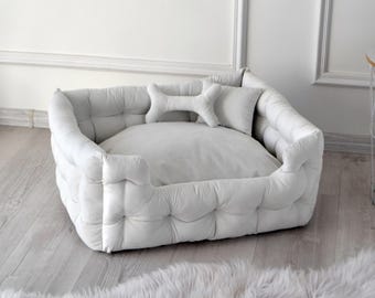May include: A white, tufted dog bed with a bone-shaped pillow. The bed is made of a soft, plush fabric and has a raised rim for added comfort.