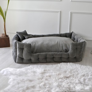 May include: A gray tufted dog bed with a removable cushion. The bed is made of a soft, plush fabric and has a raised rim for added comfort.