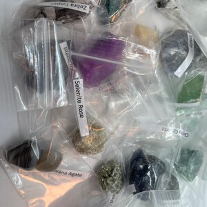 May include: A collection of various crystals and stones in individual plastic bags. The bags are labeled with the names of the stones, including Zebra Jasper, Selenite Rose, Black Tourmaline, Sodalite, Grey Quartz, and Wana Agate.